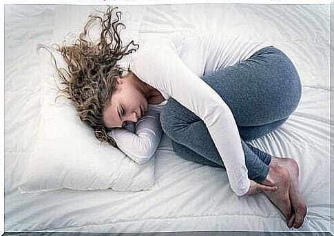 Woman lying in fetal position in bed