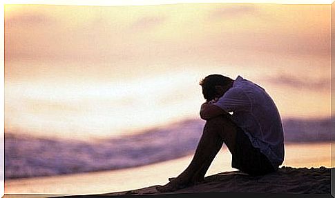 Man on beach is depressed and rests head on knees