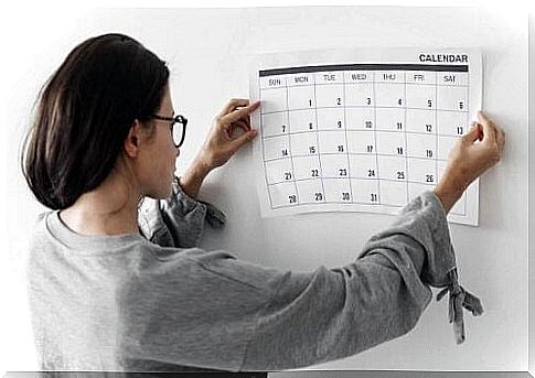 A woman puts a calendar on the wall.