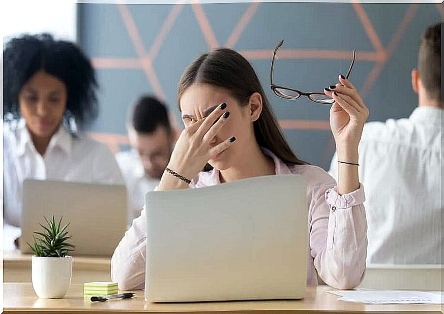 Woman behind computer scratches her eyes