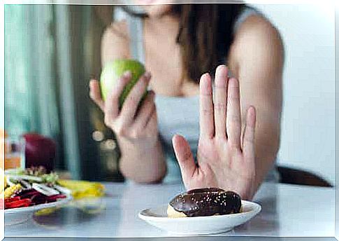 Woman with apple in hand says no to donut to reduce sugar in diet